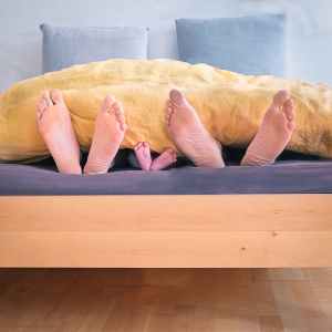 family of three lying on bed showing feet while covered with yellow blanket