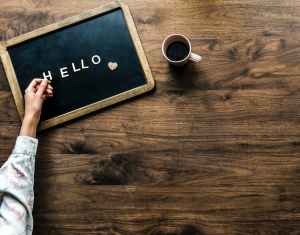 person s hand on black board with hello text beside brown mug